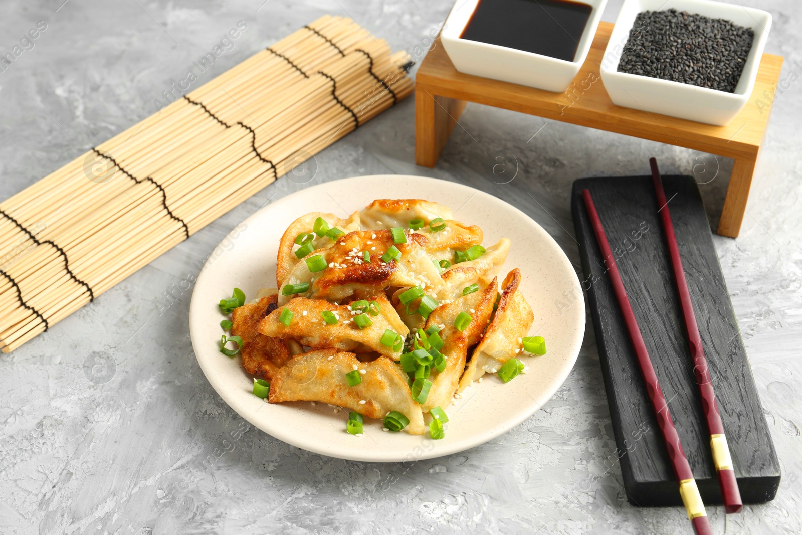 Photo of Tasty fried gyoza (dumplings), soy sauce and chopsticks on light grey table