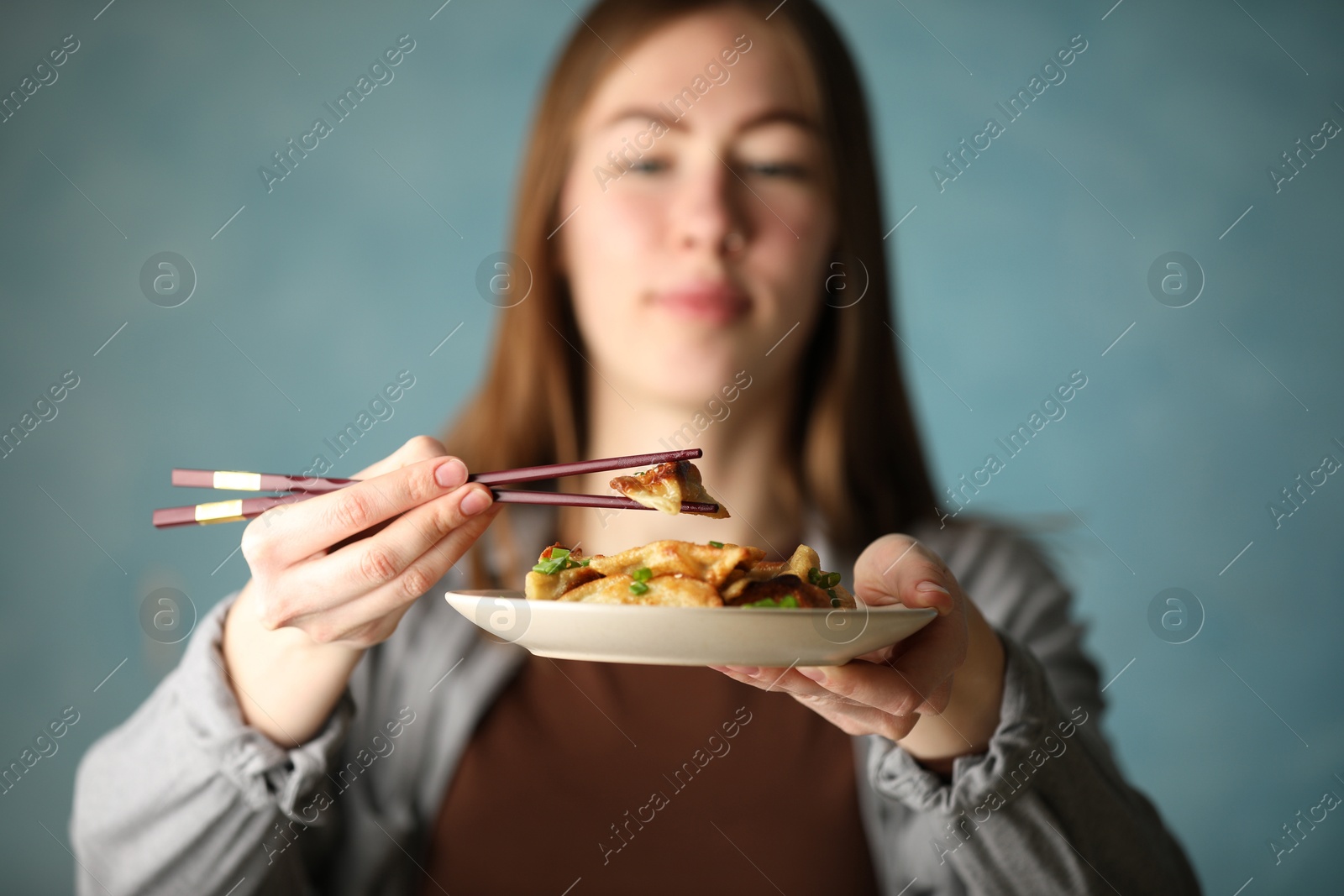 Photo of Woman holding tasty fried gyoza (dumplings) on light blue background, selective focus