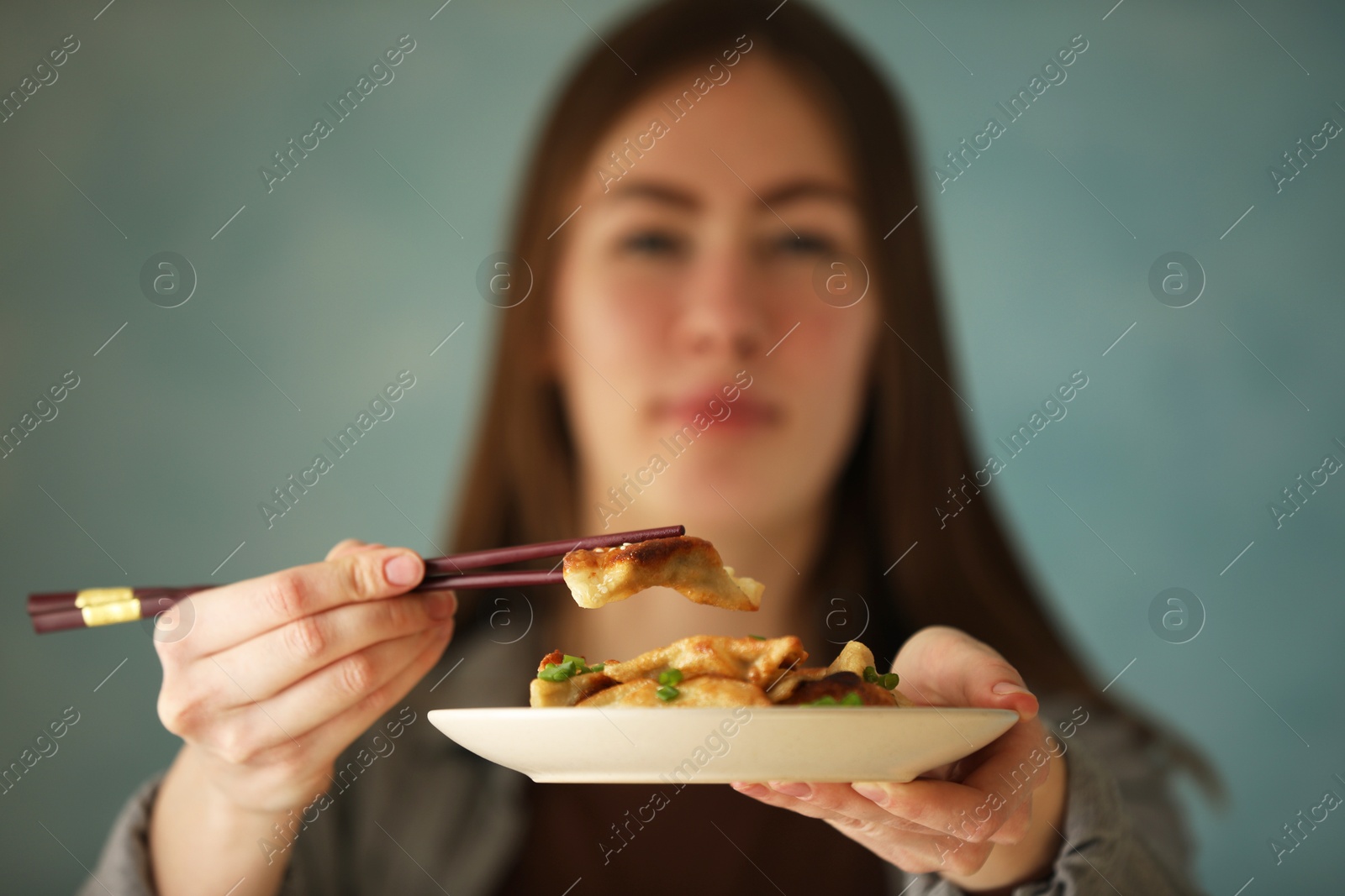 Photo of Woman holding tasty fried gyoza (dumplings) on light blue background, selective focus