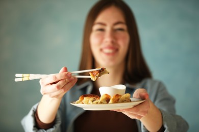 Photo of Woman holding tasty fried gyoza (dumplings) on light blue background, selective focus