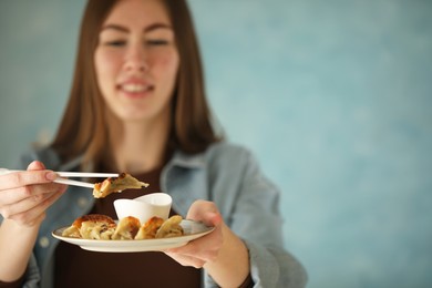 Woman holding tasty fried gyoza (dumplings) on light blue background, selective focus. Space for text