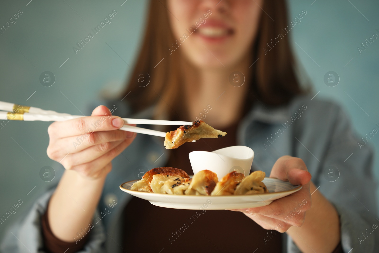 Photo of Woman holding tasty fried gyoza (dumplings) on light blue background, closeup