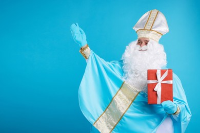 Photo of Saint Nicholas with Christmas gift on light blue background, space for text