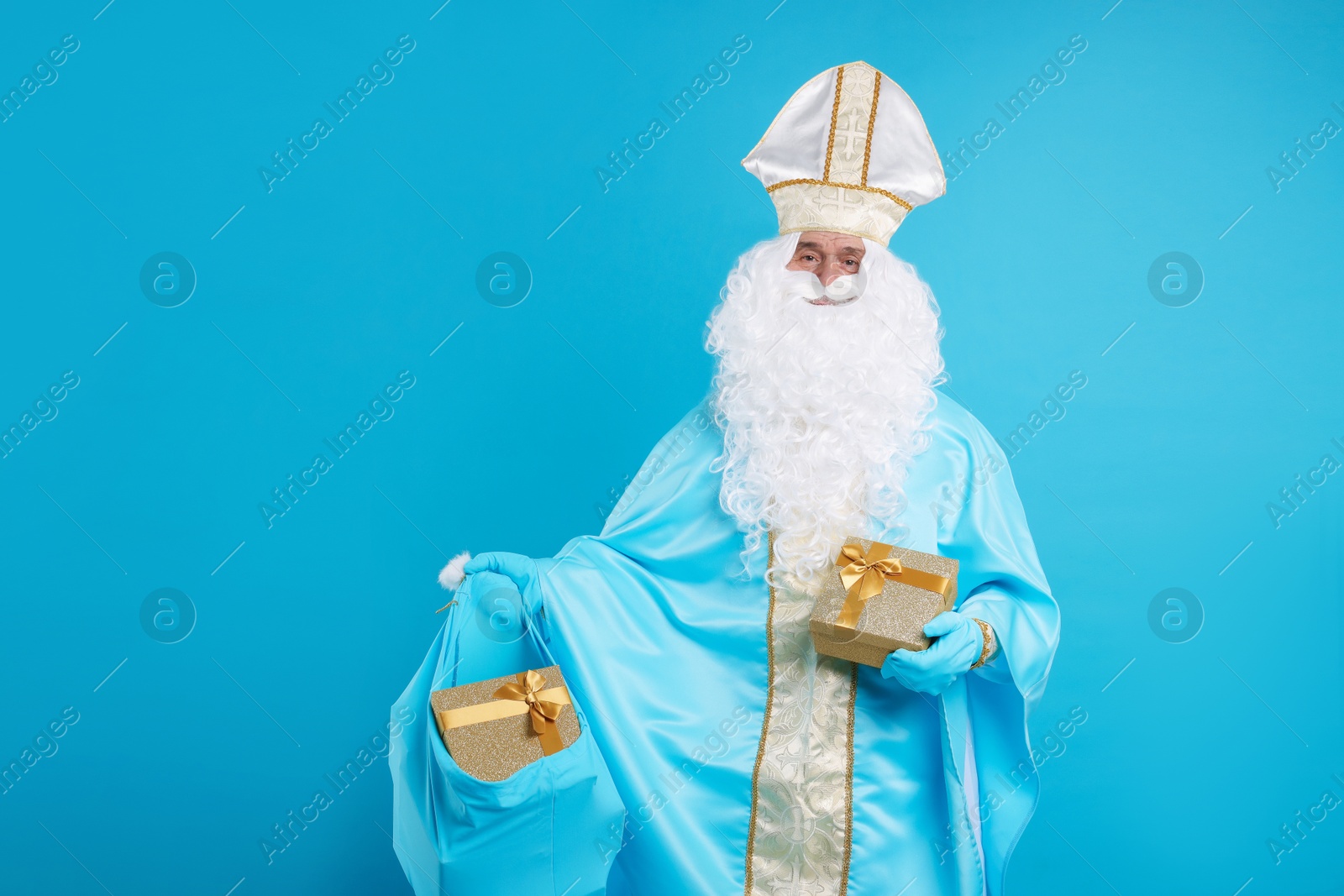 Photo of Saint Nicholas with bag of Christmas gifts on light blue background