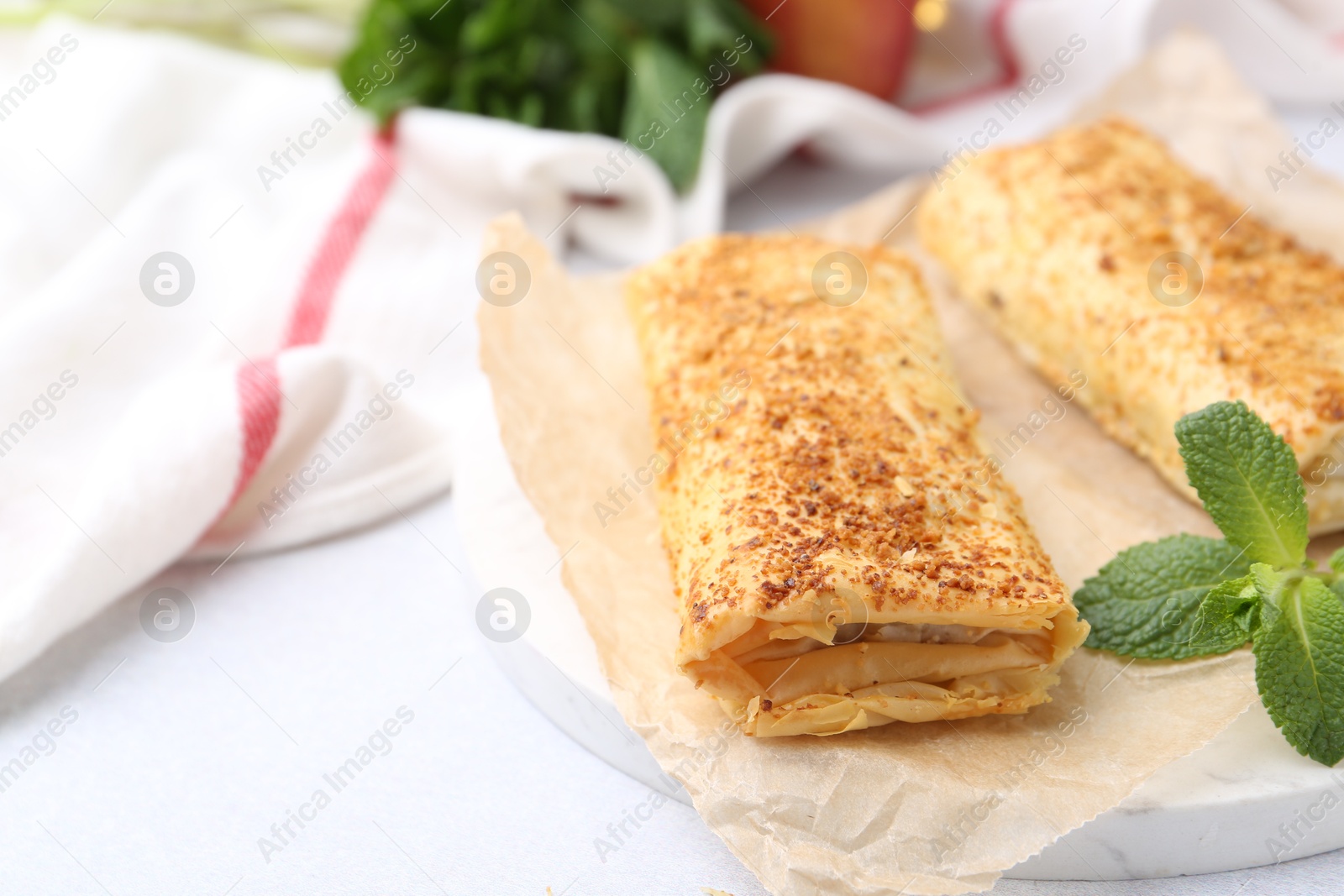 Photo of Tasty apple strudels and mint on light table, closeup. Space for text