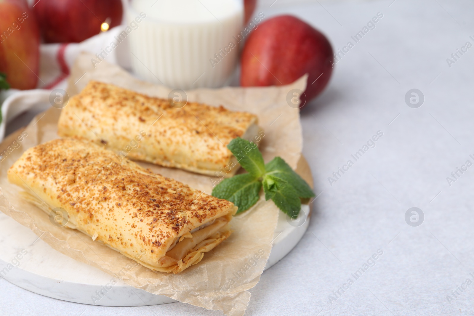 Photo of Tasty apple strudels, mint, fruits and milk on light table, closeup. Space for text