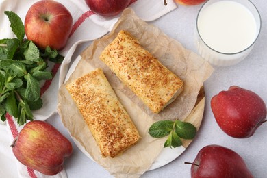 Photo of Tasty apple strudels, mint, fruits and milk on light table, flat lay