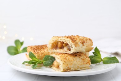 Photo of Tasty apple strudels and mint on white table, closeup