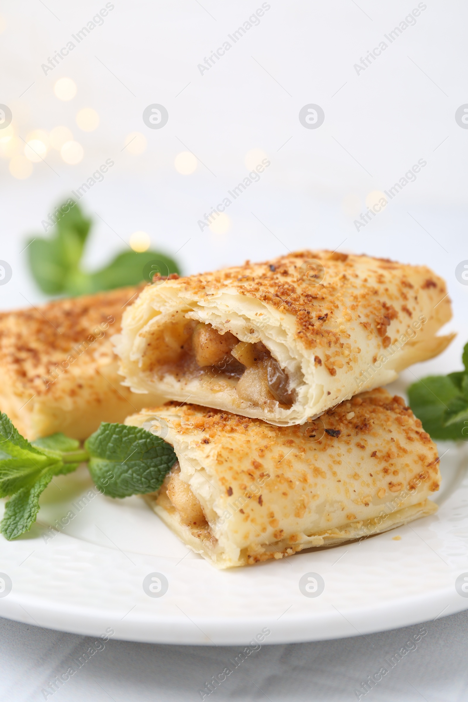 Photo of Pieces of tasty apple strudel and mint on white table, closeup