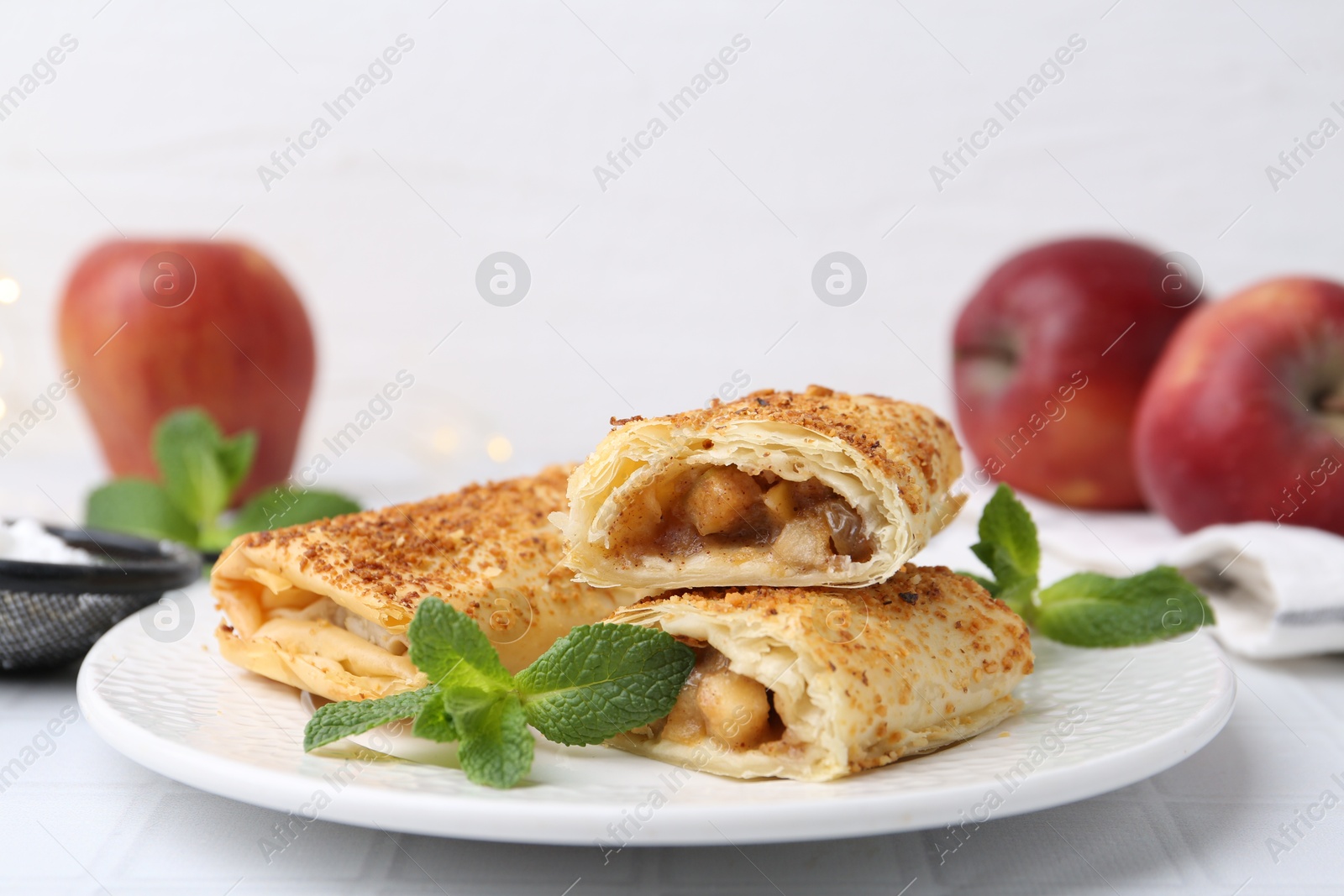 Photo of Tasty apple strudels, mint and fruits on white table, closeup