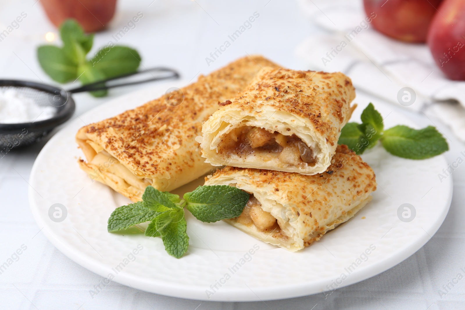 Photo of Tasty apple strudels and mint on white table, closeup