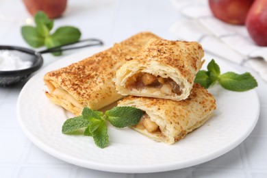 Photo of Tasty apple strudels and mint on white table, closeup