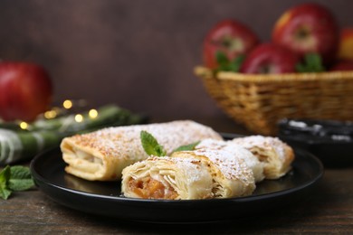 Photo of Tasty apple strudels with powdered sugar and mint on wooden table, closeup