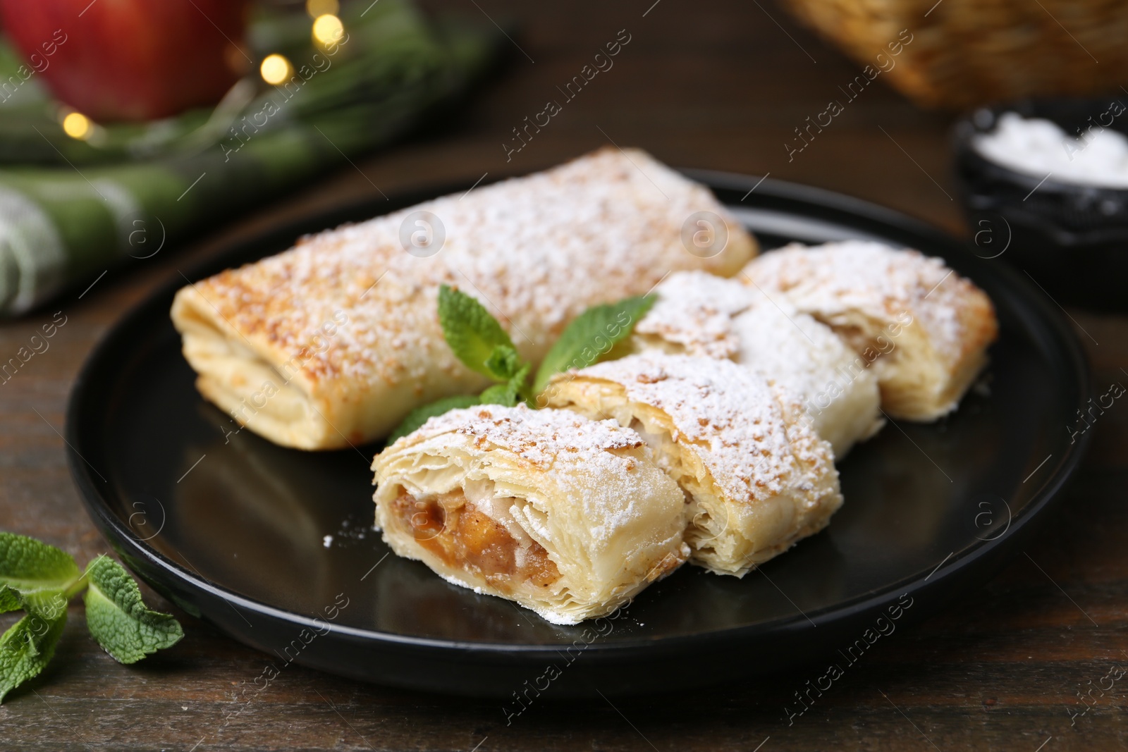 Photo of Tasty apple strudels with powdered sugar and mint on wooden table, closeup