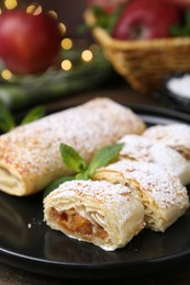 Photo of Tasty apple strudels with powdered sugar and mint on table, closeup