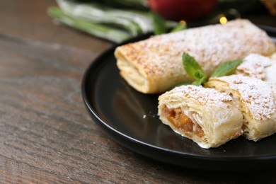 Photo of Tasty apple strudels with powdered sugar and mint on wooden table, closeup. Space for text