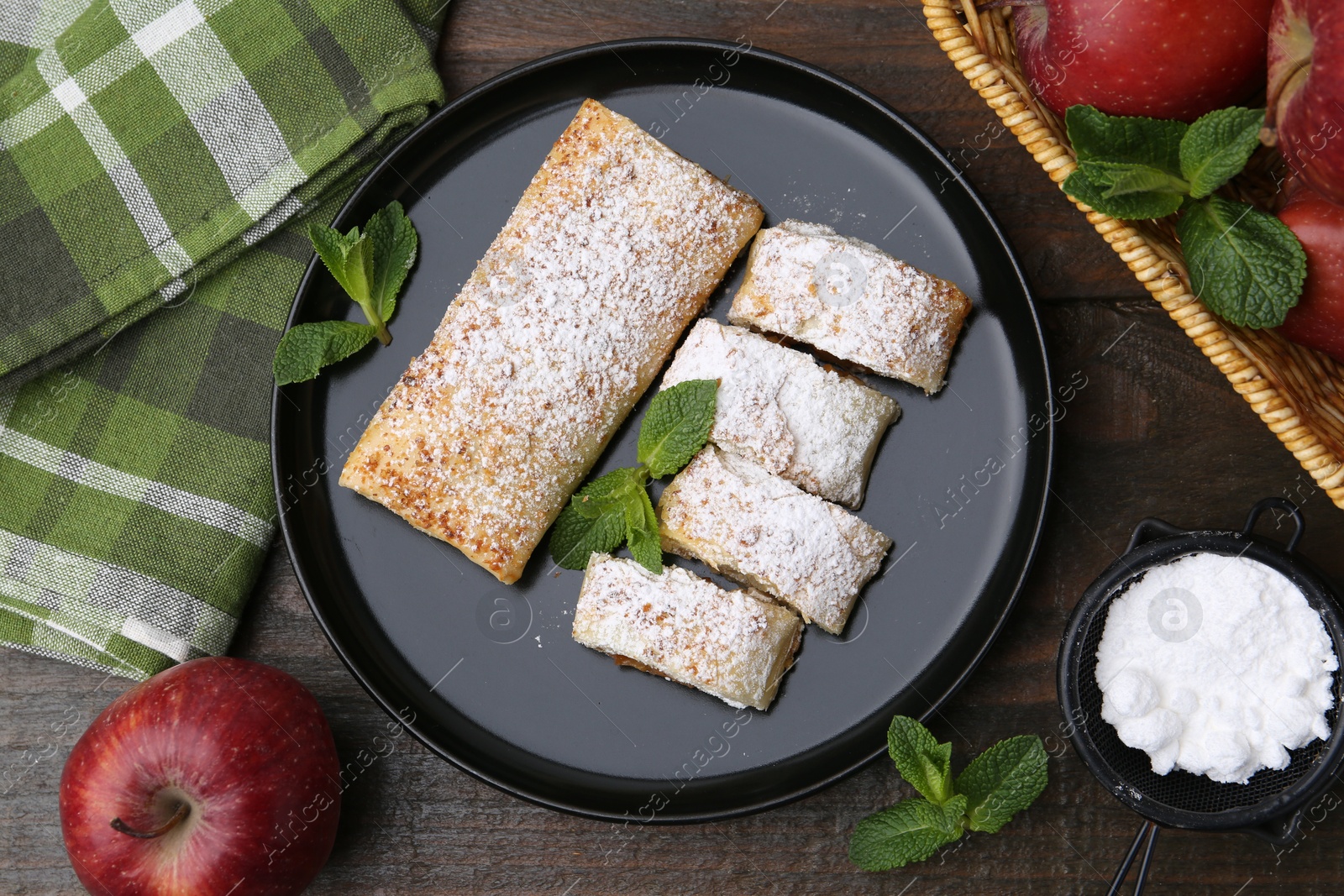 Photo of Tasty apple strudels with powdered sugar, mint and fruits on wooden table, flat lay