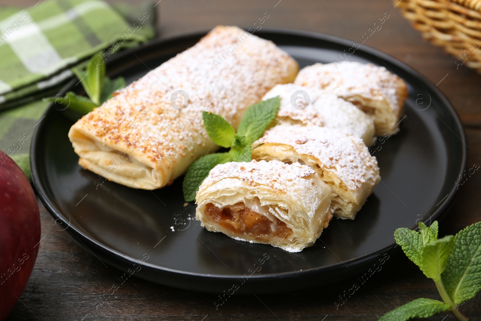 Photo of Tasty apple strudels with powdered sugar and mint on wooden table, closeup