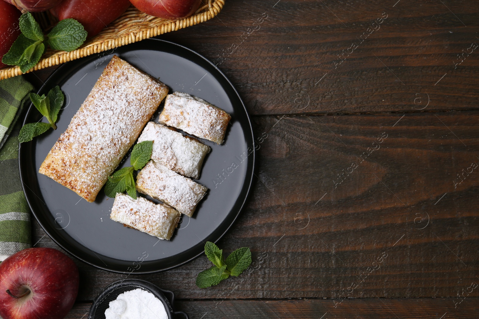 Photo of Tasty apple strudels with powdered sugar, mint and fruits on wooden table, flat lay. Space for text