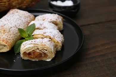 Photo of Tasty apple strudels with powdered sugar and mint on wooden table, closeup. Space for text