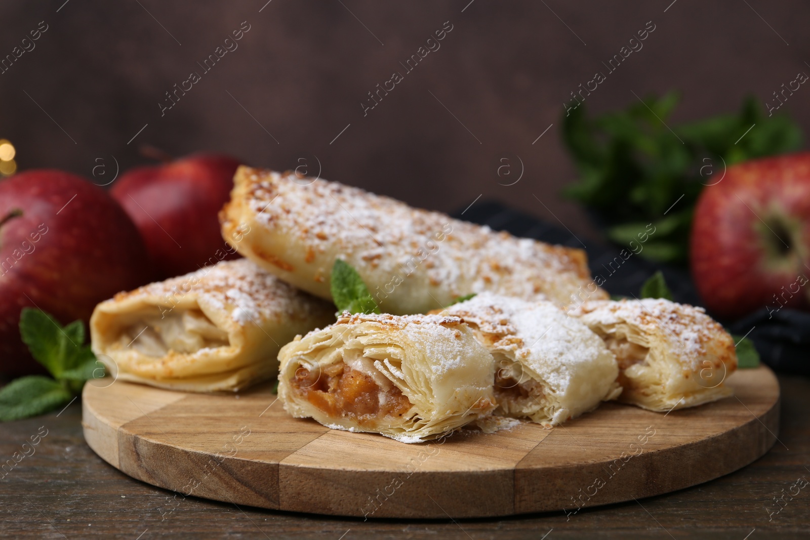 Photo of Tasty apple strudels with powdered sugar, mint and fruits on wooden table, closeup