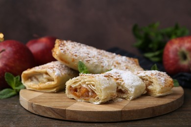 Photo of Tasty apple strudels with powdered sugar, mint and fruits on wooden table, closeup