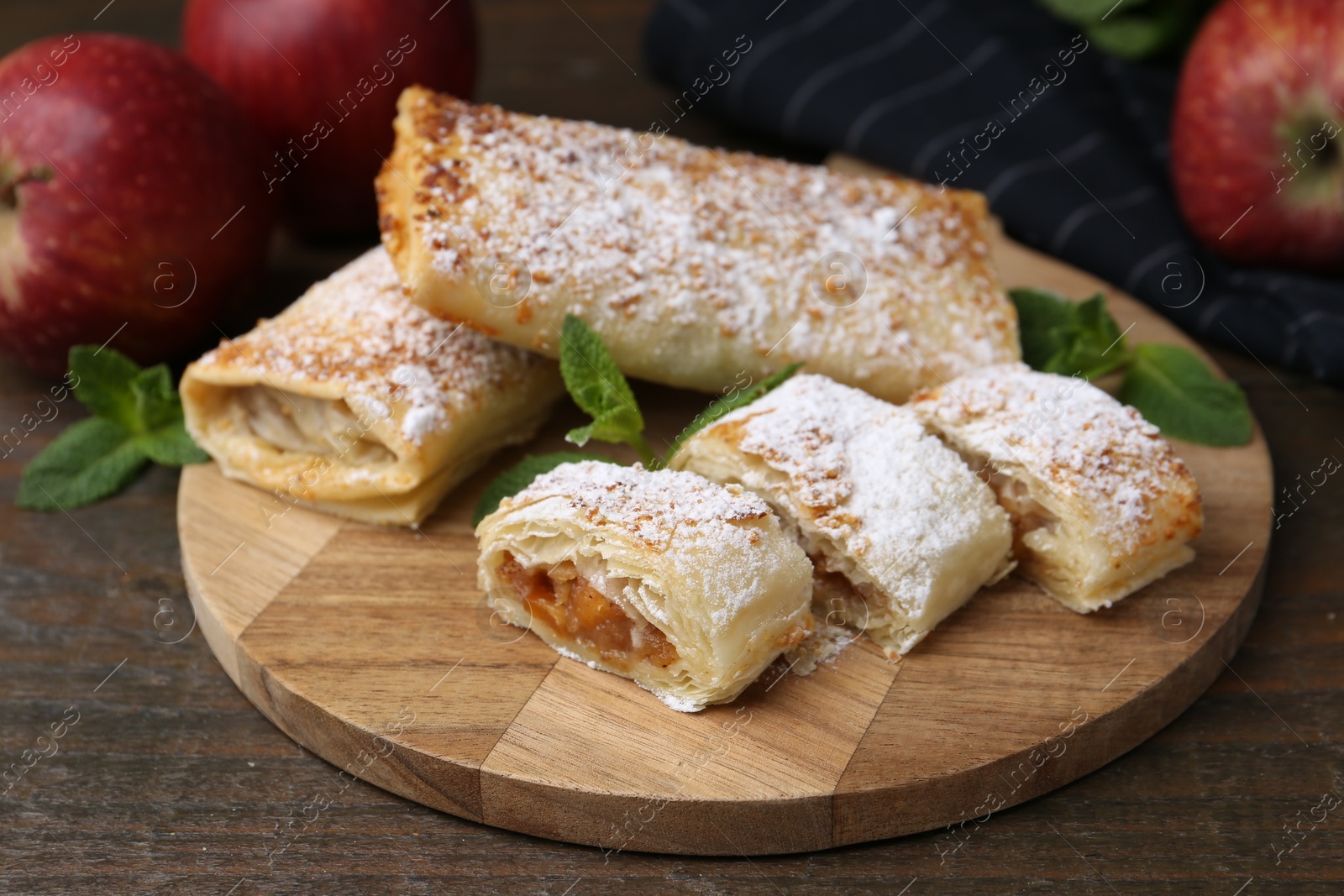 Photo of Tasty apple strudels with powdered sugar, mint and fruits on wooden table, closeup