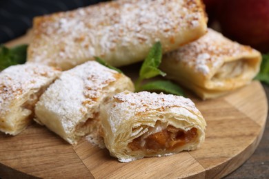 Photo of Tasty apple strudels with powdered sugar and mint on table, closeup