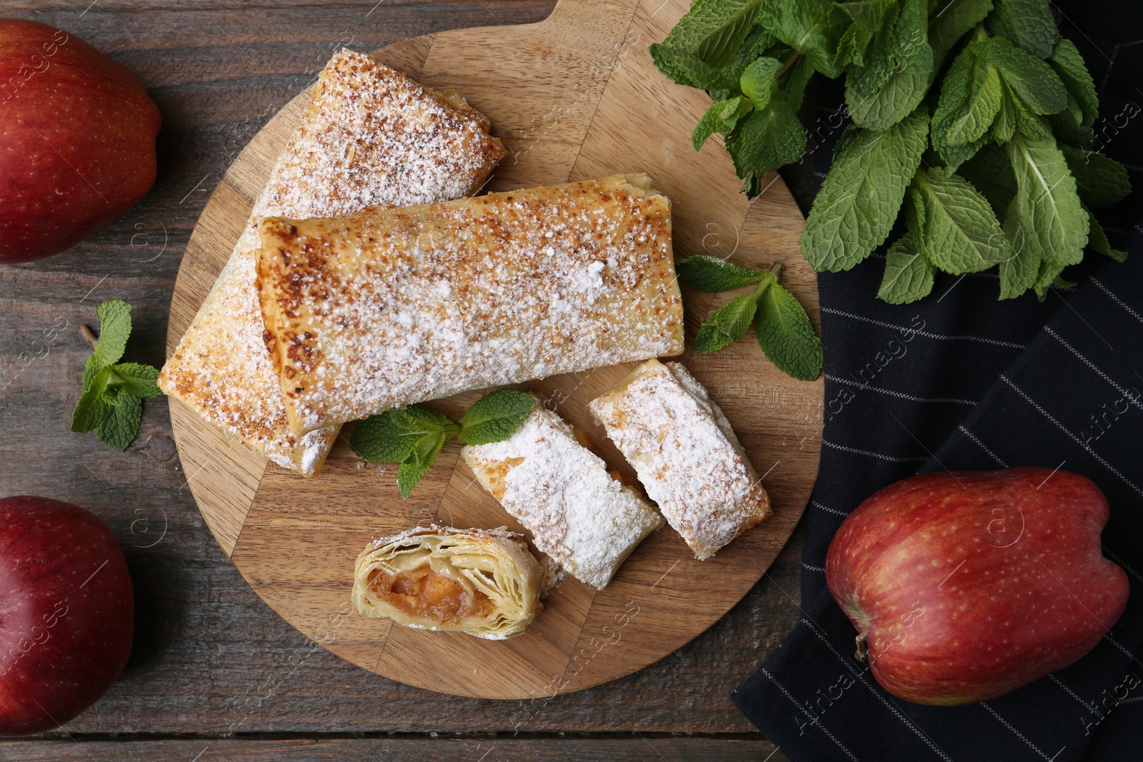 Photo of Tasty apple strudels with powdered sugar, mint and fruits on wooden table, flat lay