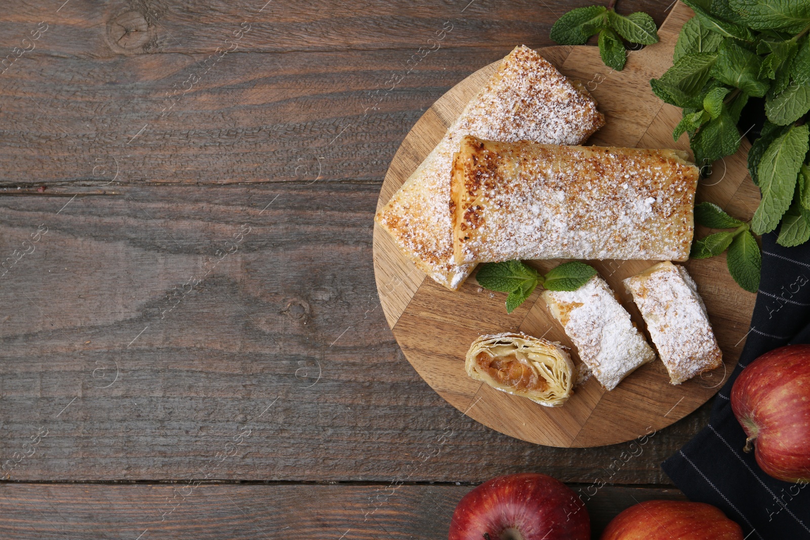 Photo of Tasty apple strudels with powdered sugar, mint and fruits on wooden table, flat lay. Space for text