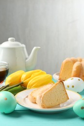 Photo of Pieces of delicious bundt cake, Easter eggs, tulips and tea on light blue wooden table