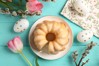 Photo of Delicious bundt cake, Easter eggs, willow branches and tulips on light blue wooden table, flat lay