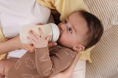 Photo of Mother feeding her little baby from bottle indoors, closeup