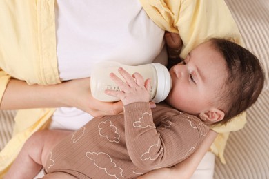 Photo of Mother feeding her little baby from bottle indoors, closeup