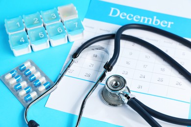 Photo of Stethoscope, calendar and pills on light blue background, closeup
