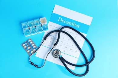 Photo of Stethoscope, calendar and pills on light blue background, flat lay