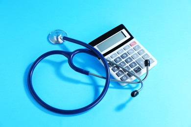 Photo of Stethoscope and calculator on light blue background, above view