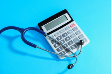 Photo of Stethoscope and calculator on light blue background, above view