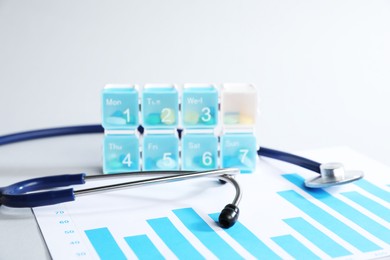 Photo of Stethoscope, chart and pills in organizer on light background, closeup