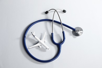 Photo of Stethoscope and airplane model on light background, flat lay