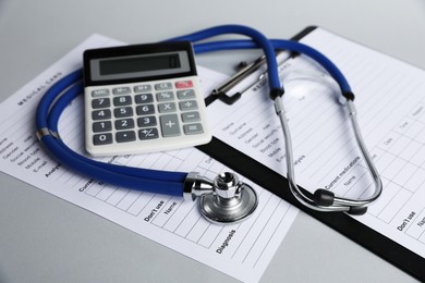 Photo of Stethoscope, medical card forms and calculator on gray background, closeup