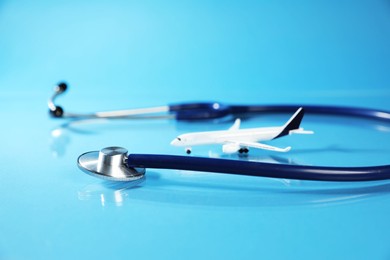Photo of Stethoscope and airplane model on light blue background, closeup