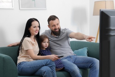 Photo of Cute little girl and her parents watching tv together at home