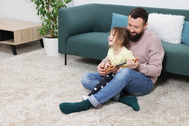 Photo of Father and his cute little daughter playing ukulele at home