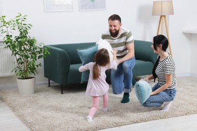 Photo of Cute little girl and her parents having fun while fighting with pillows at home