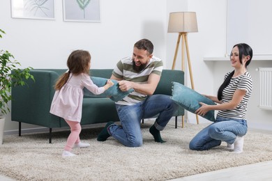 Photo of Cute little girl and her parents having fun while fighting with pillows at home