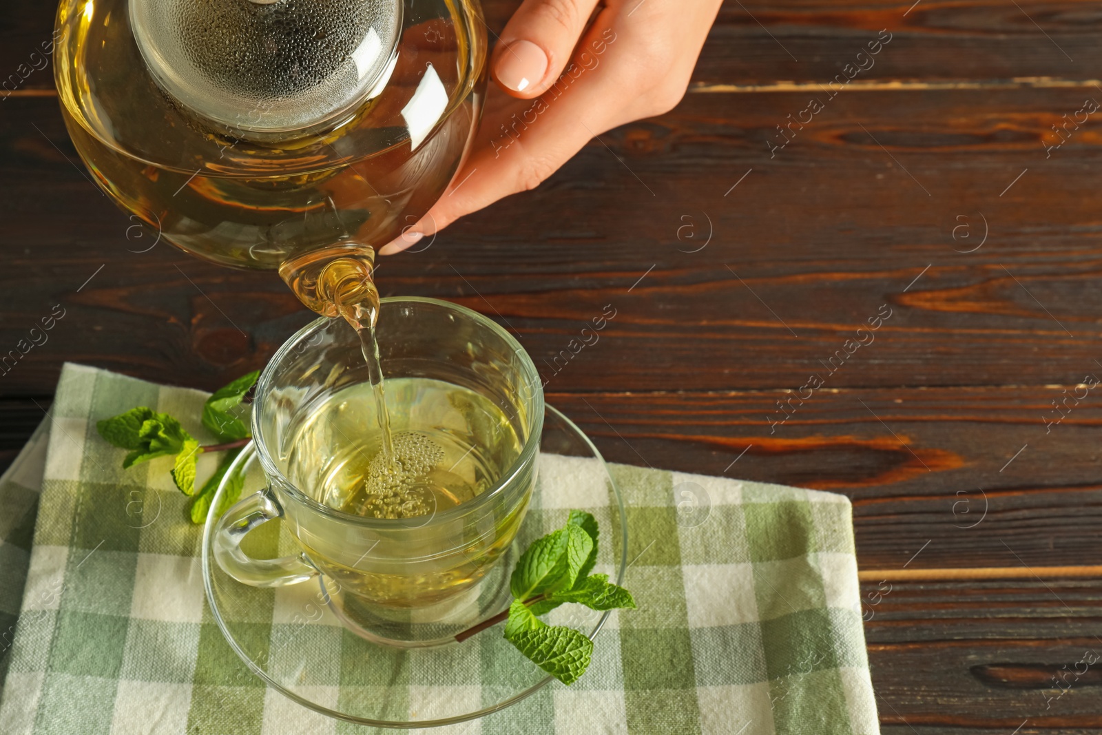 Woman pouring freshly brewed tea from teapot into cup at wooden table, closeup Photo of Woman pouring freshly brewed tea from teapot into cup at wooden table, closeup