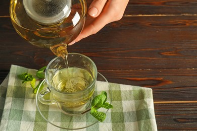 Photo of Woman pouring freshly brewed tea from teapot into cup at wooden table, closeup