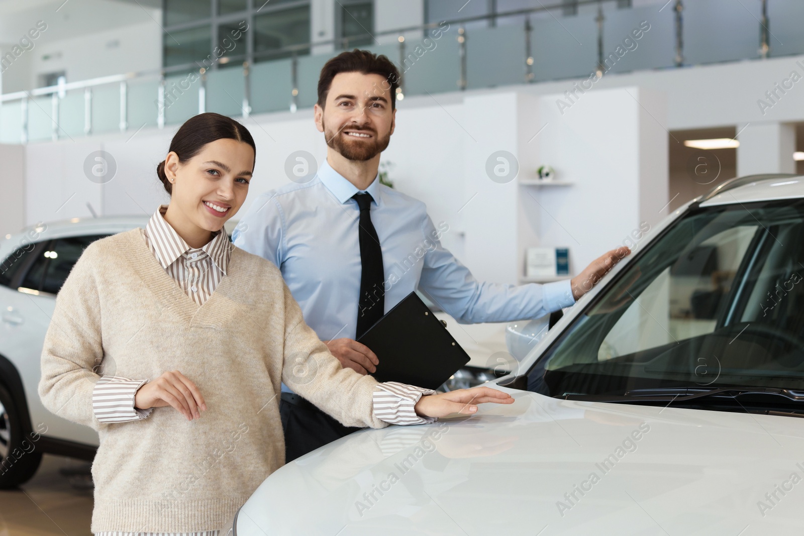 Photo of Happy salesman and client near new car in salon