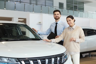 Photo of Happy salesman and client near new car in salon